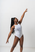 Load image into Gallery viewer, A dancer in a sleek white leotard poses gracefully with one arm extended overhead, showcasing artistic movement
