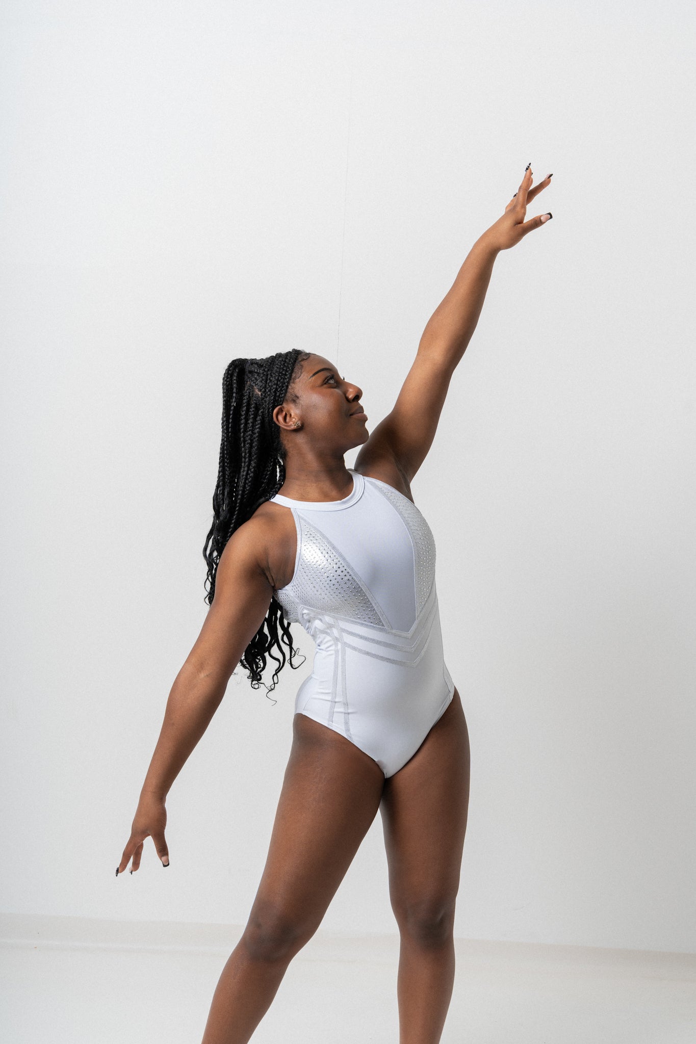 A dancer in a sleek white leotard poses gracefully with one arm extended overhead, showcasing artistic movement