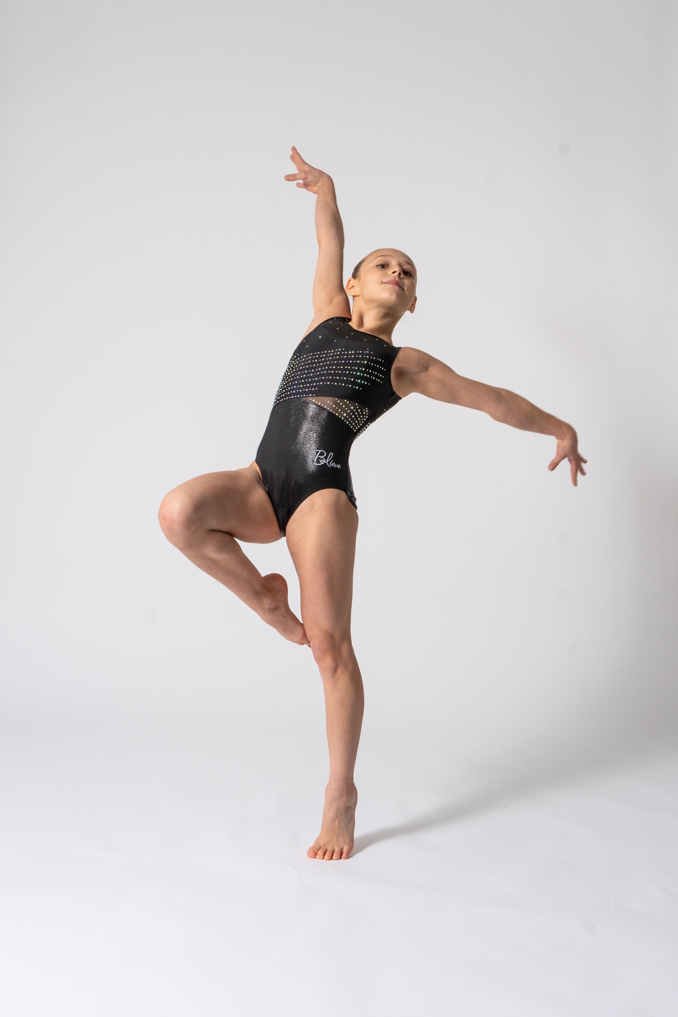 A young gymnast performing a dance pose in a black leotard with multicolored sequins