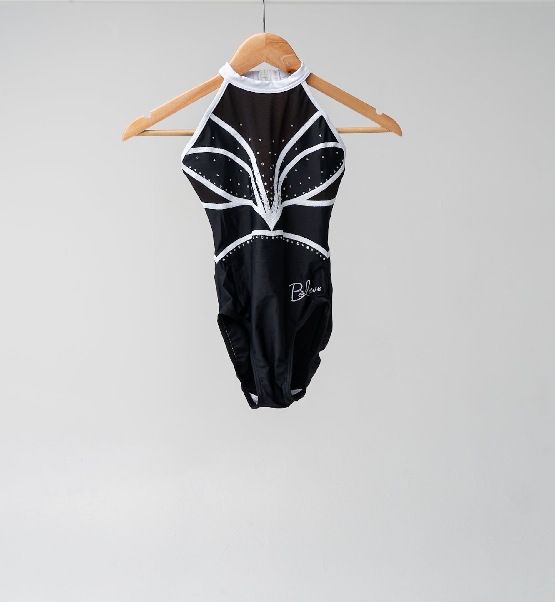 Black and white gymnastics leotard with decorative rhinestones hanging on a wooden hange