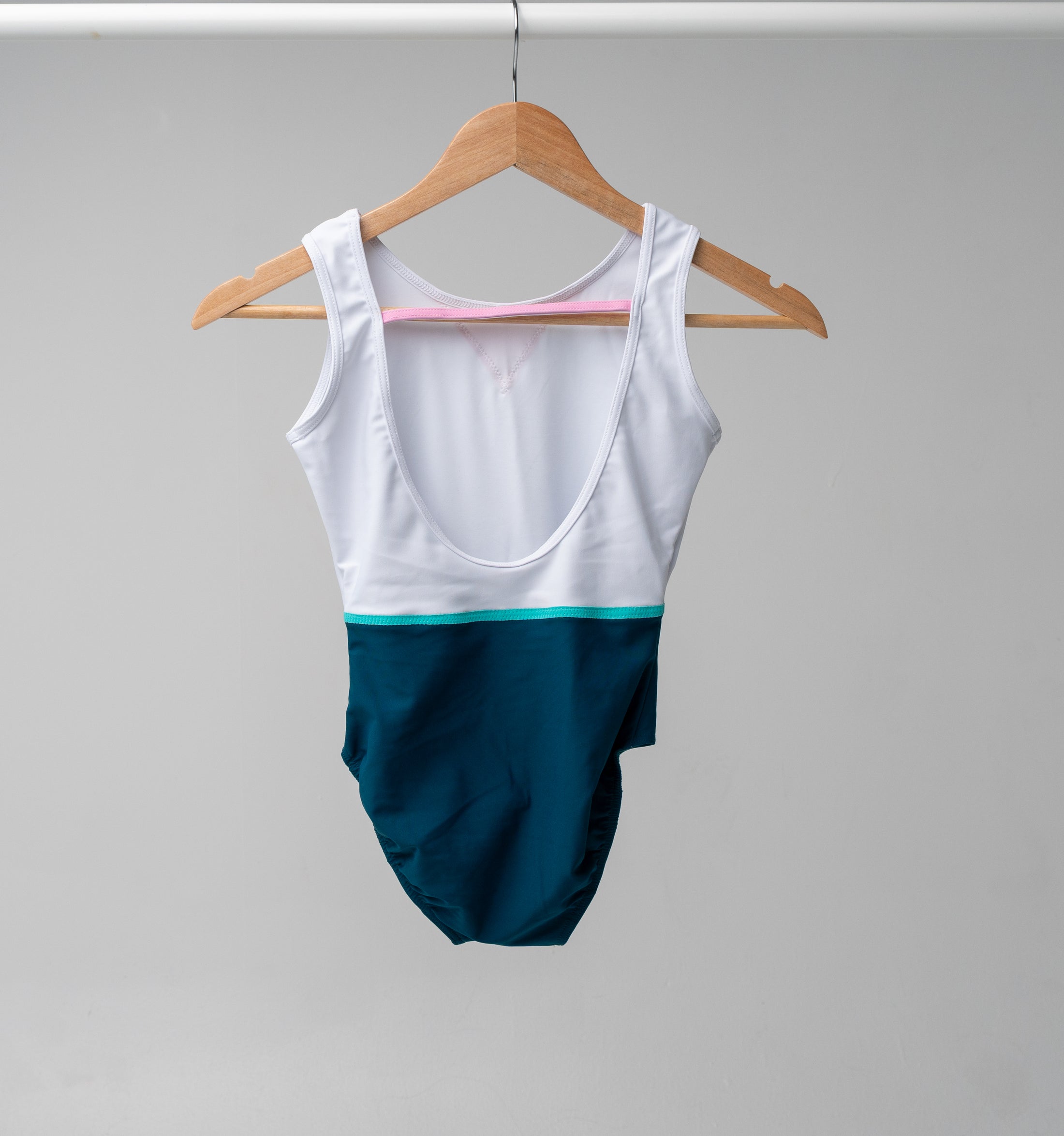 The back of a White and teal leotard hanging on a wooden hanger