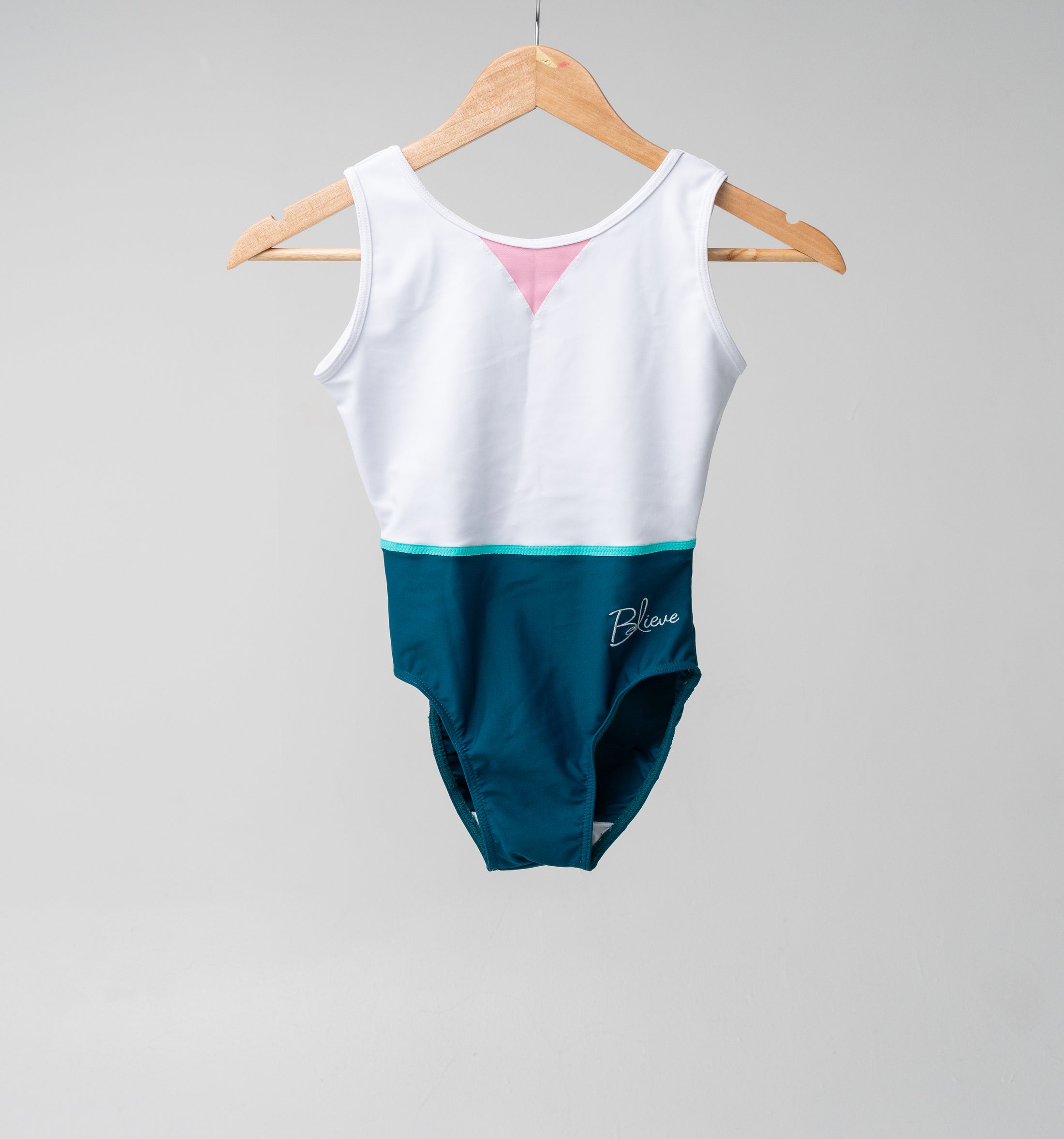 Colorful leotard hanging on a wooden hanger, featuring a white top and teal bottom with a pink accent.